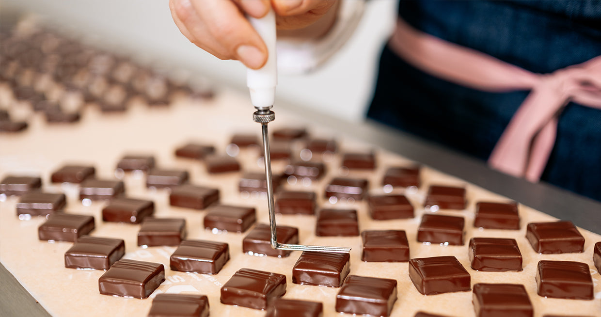 Rows of Ginger Elizabeth Chocolates chocolate bobons being stamped by hand with custom instrument. 