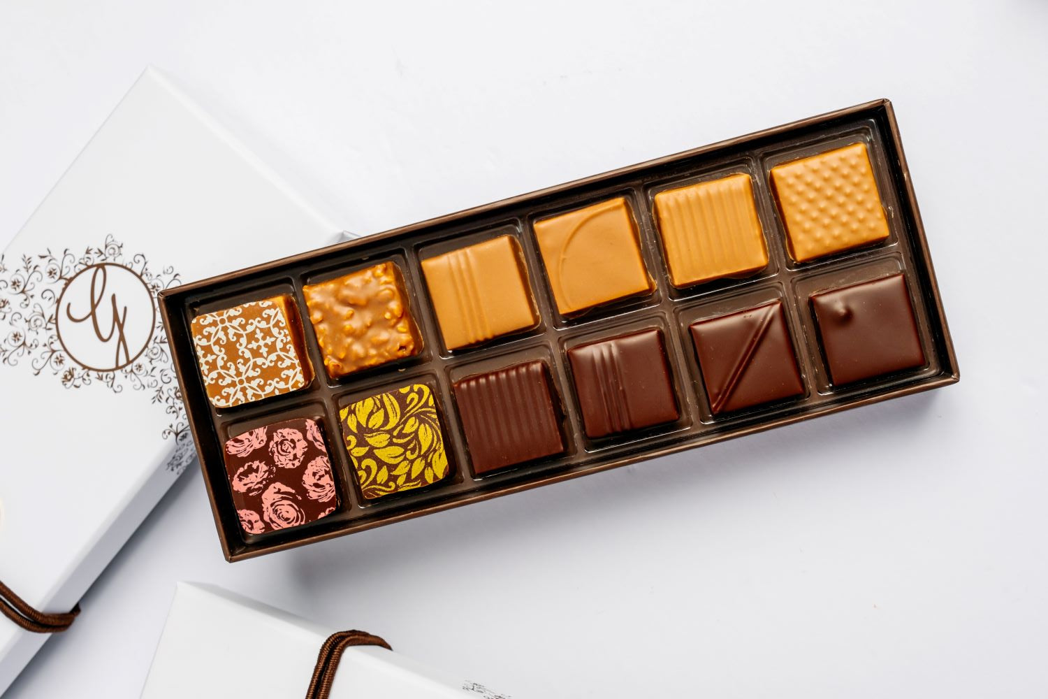 open full 12-piece box of chocolates arranged with closed box beneath on white background