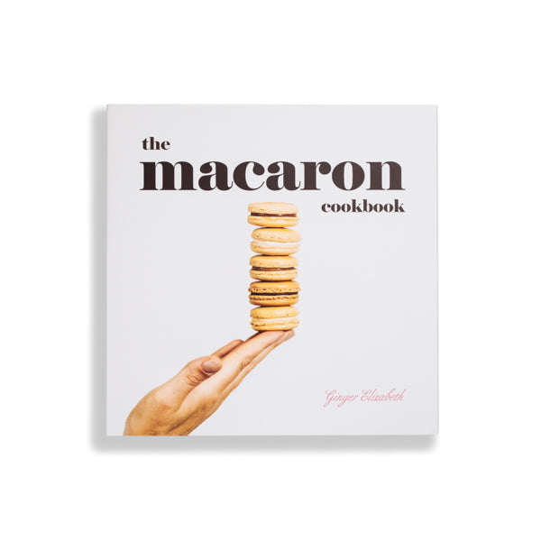 The  Macaron Cookbook with cover art featuring a hand balancing a stack of macaron cookies on white background 