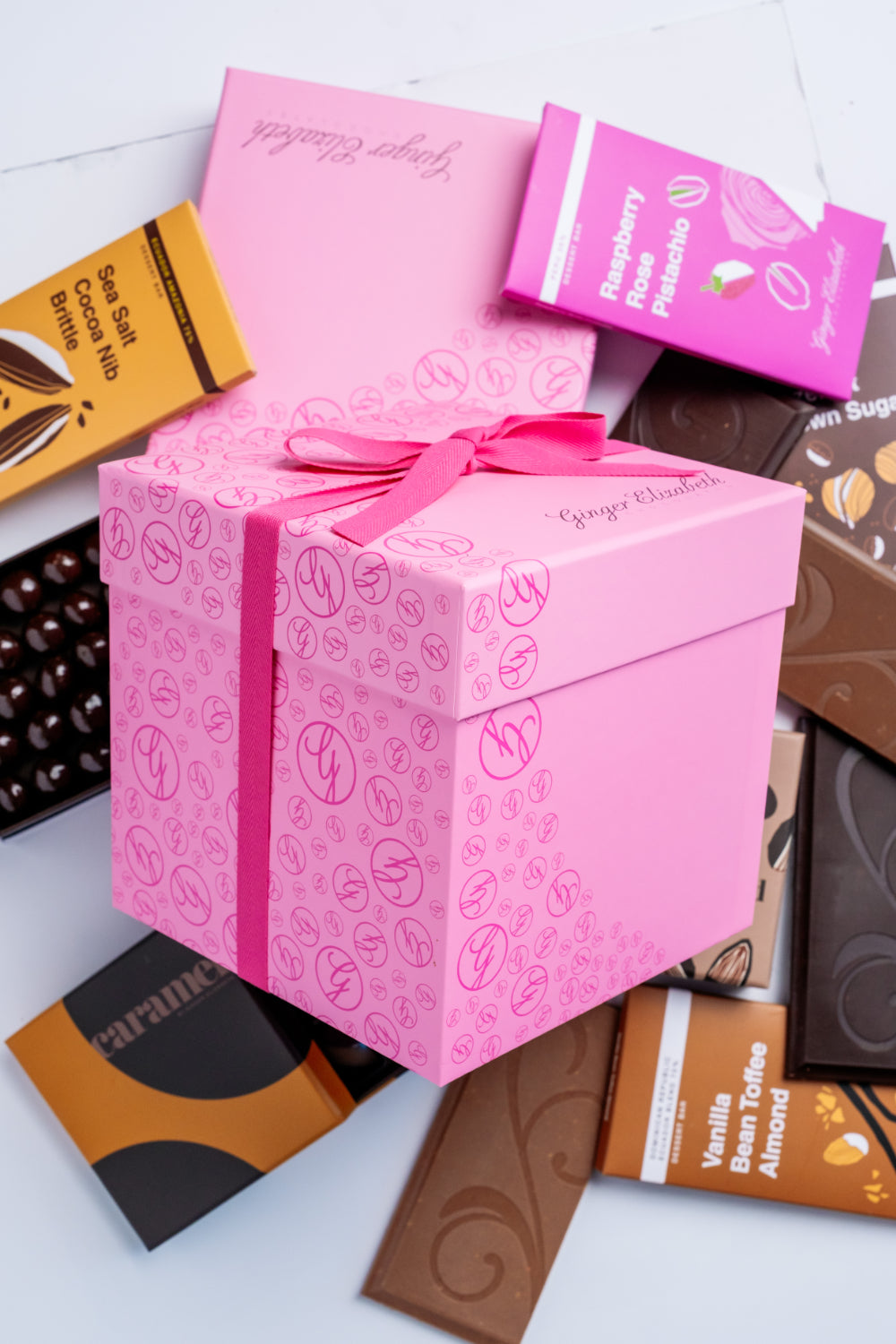 Pink gift box with a bow surrounded by various chocolate bars on a light background