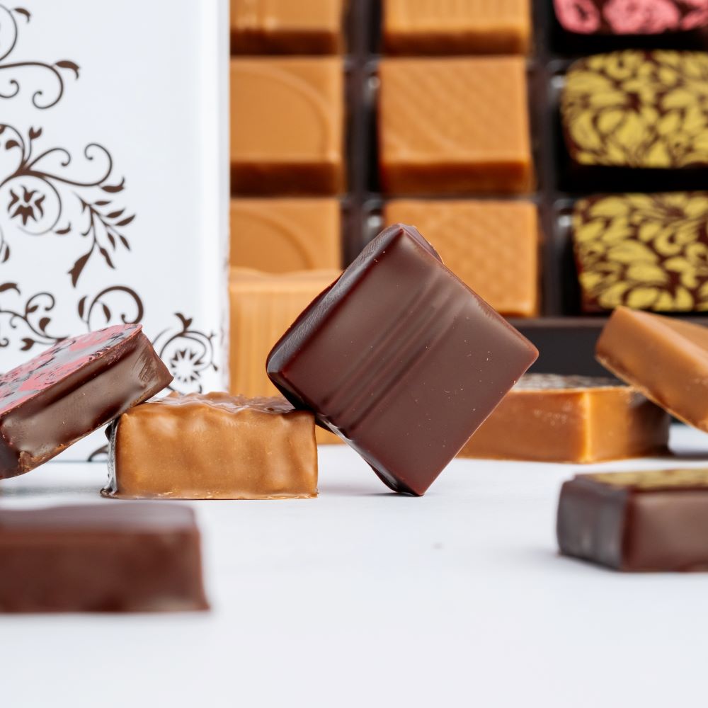square chocolates arranged in front of open and closed box on white background