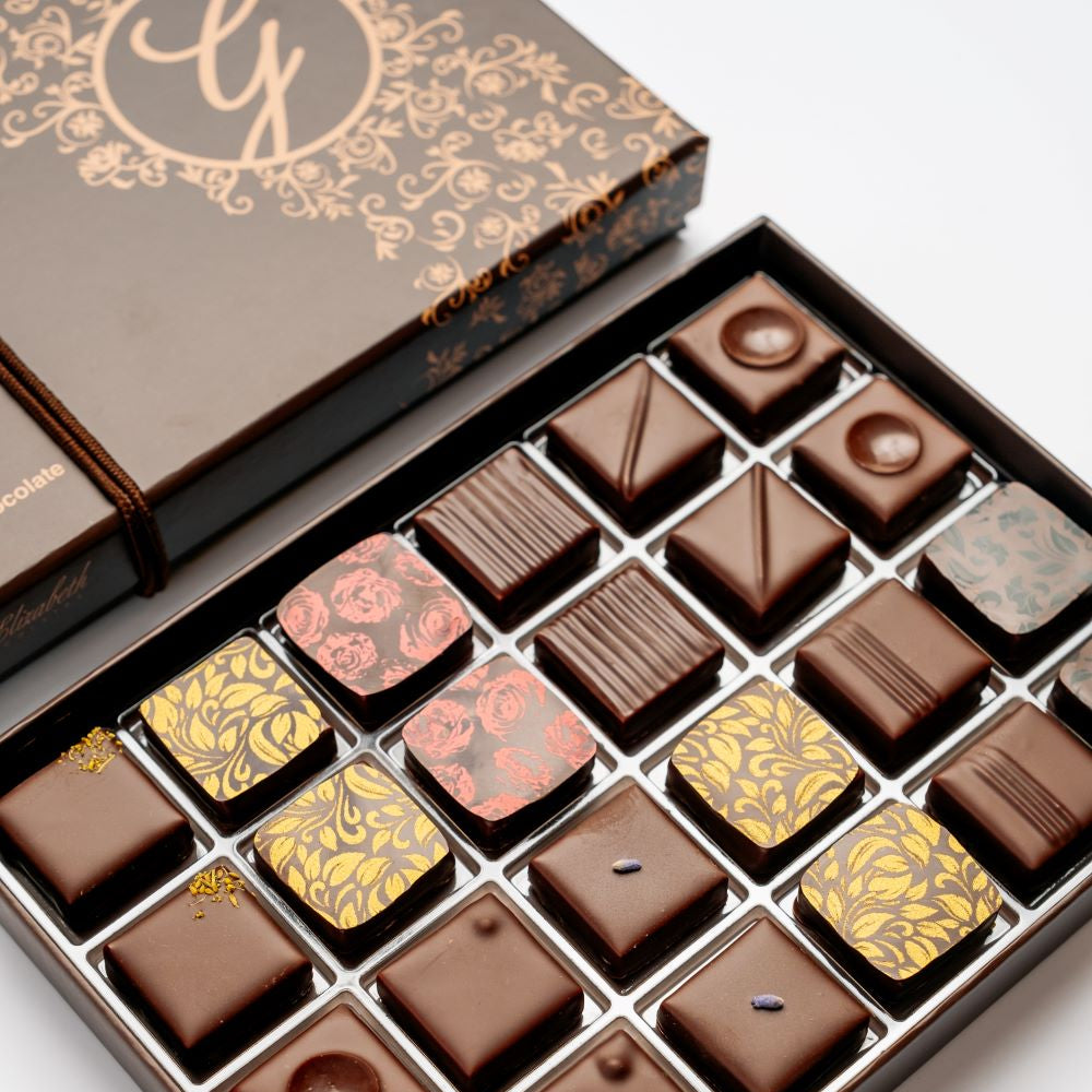 open 24-piece box of dark chocolate bonbons under closed box arranged diagonally on white background