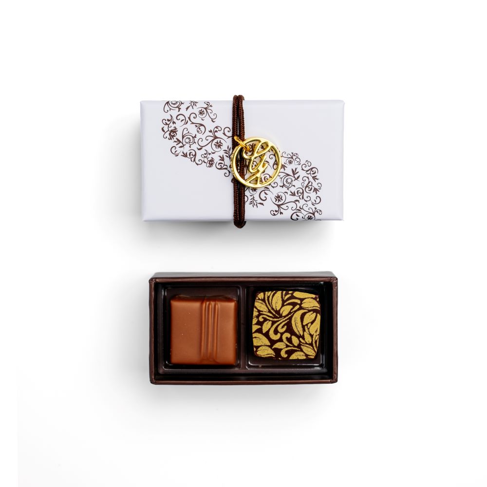 open 2 piece chocolate box with palet d'or and creme fraiche bonbons and closed box above with G charm on white background