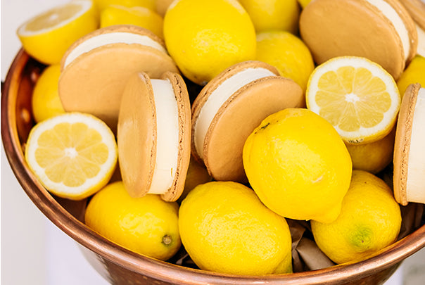 frozen macaron sandwiches arranged in copper bowl with whole and halved lemons. 