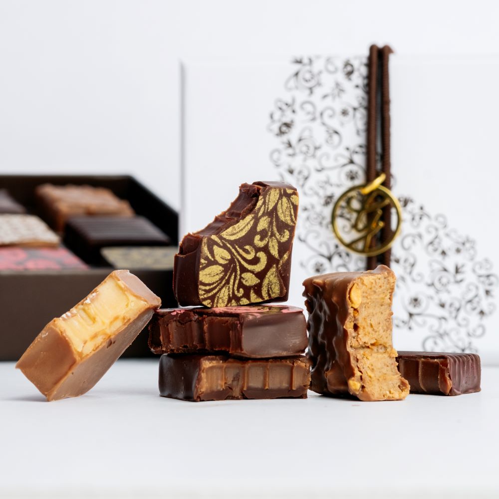 image of square chocolates arranged in front of open and closed boxes on white background 