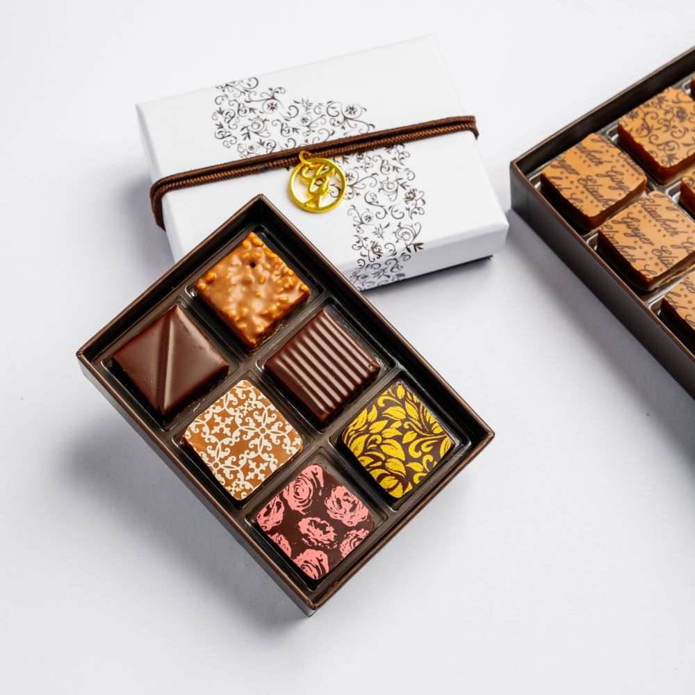 image of open, full 6-piece chocolate box arranged with open and closed boxes on white background