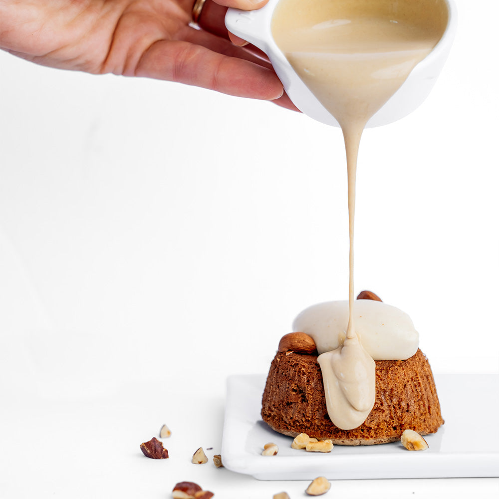 Ginger Elizabeth Chocolates chocolate molten souffle dessert with nut pieces and pour over of cream on white background