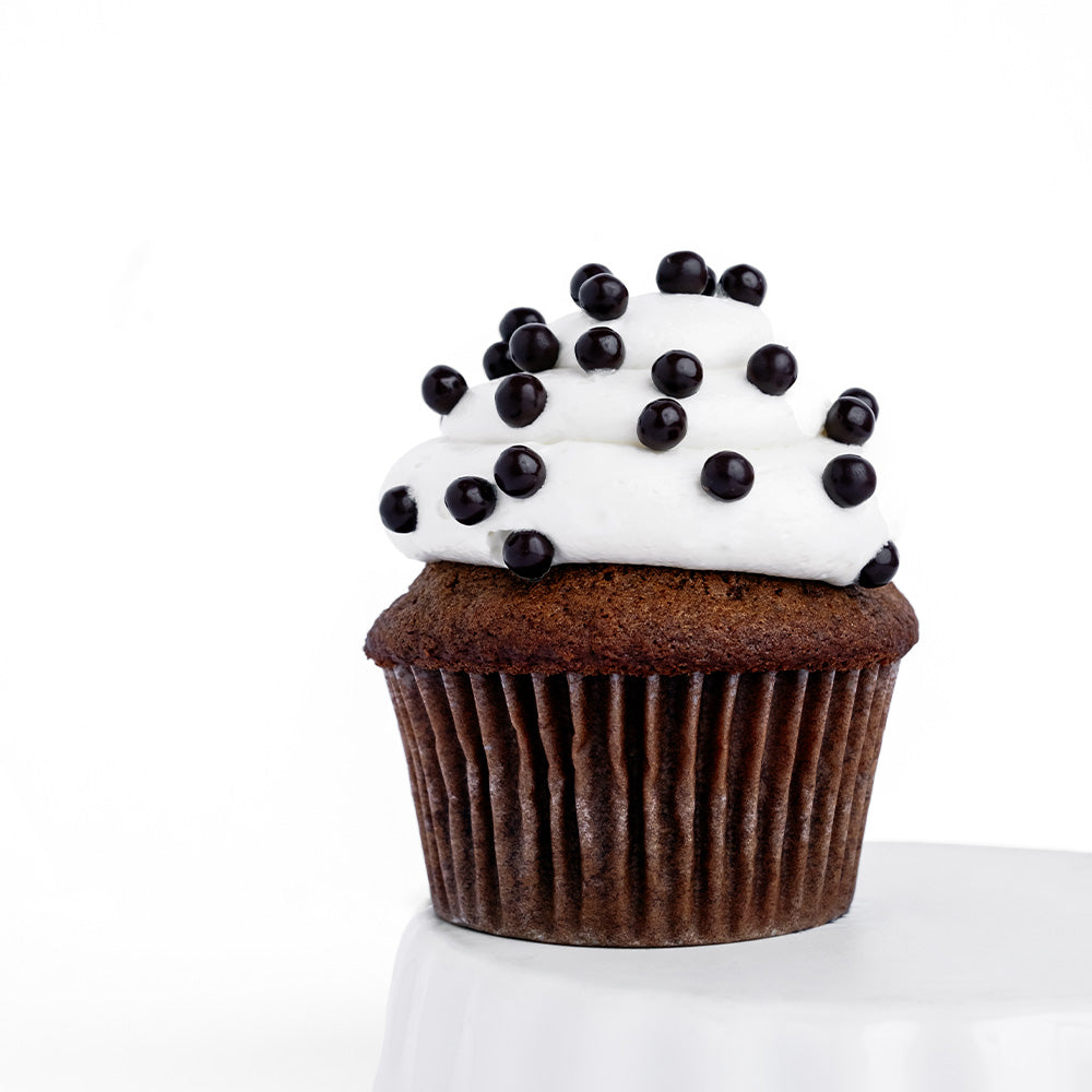Ginger Elizabeth Chocolates Red Velvet Cupcake with white frosting sprinkled with chocolate balls on white ramekin on white background