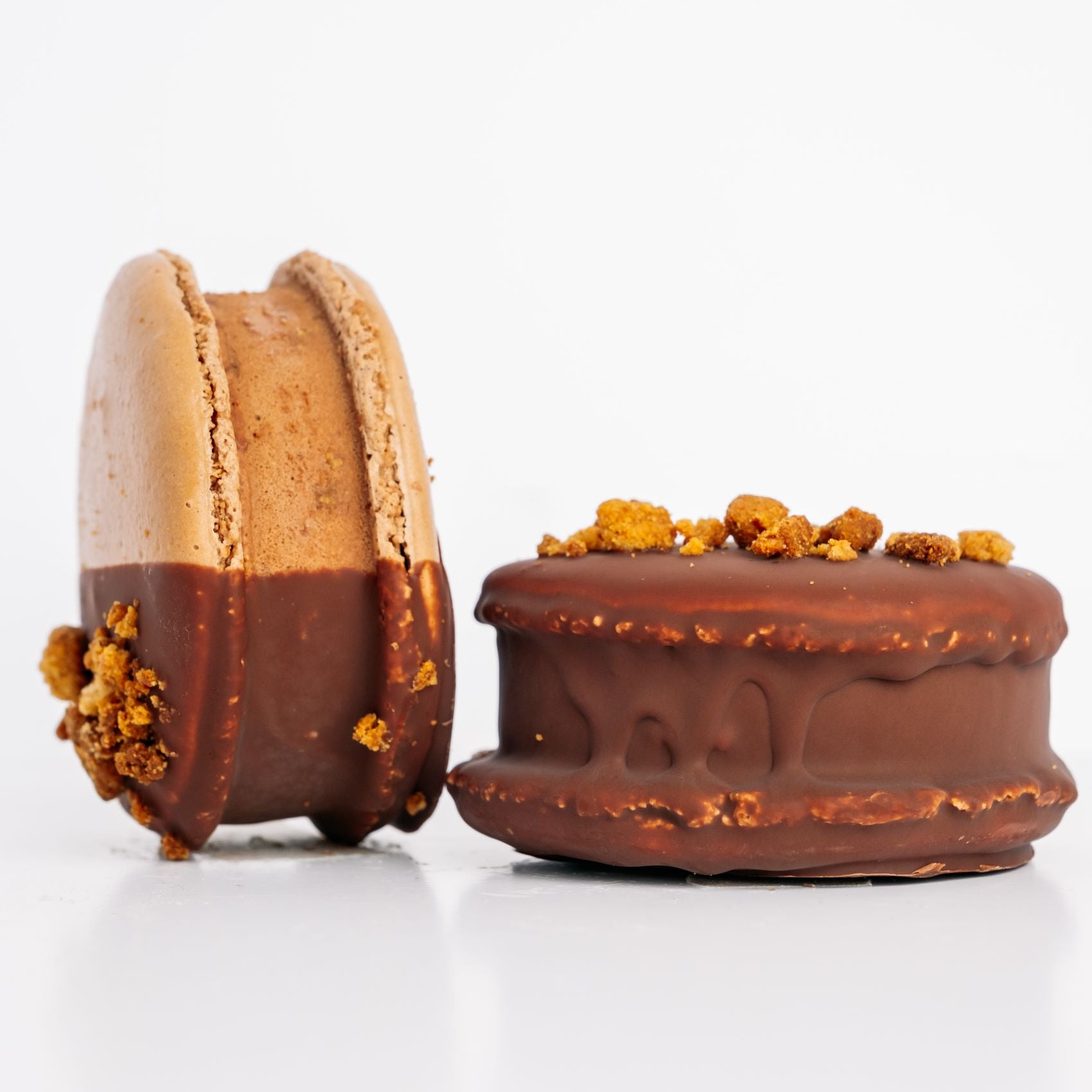 Two chocolate-dipped macaron ice cream sandwiches with crumb toppings on a white background