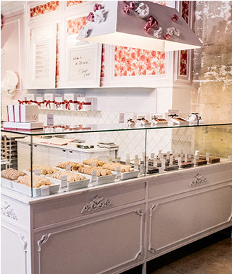 Store interior wwith cabinet displaying macarons and chocolates in fore ground. 