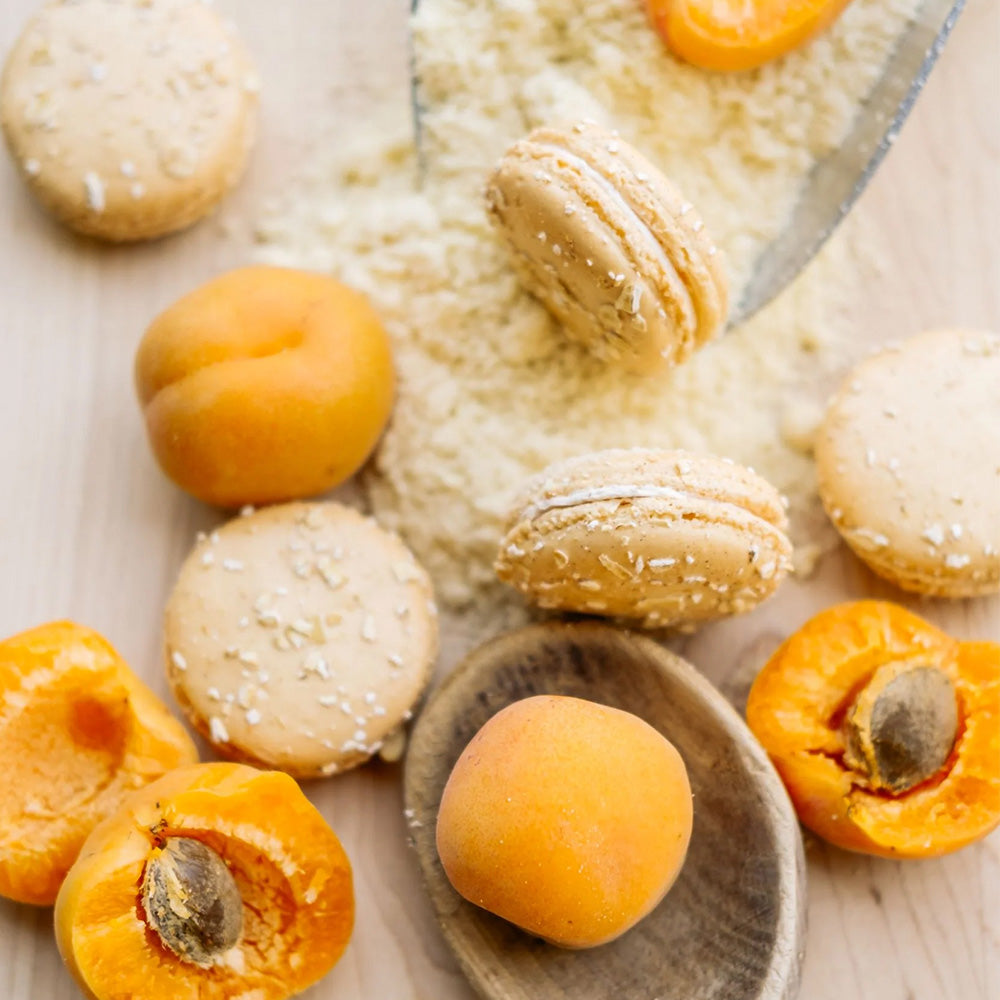 Ginger Elizabeth Chocolates Apricot Cobbler Macarons with Fresh apricots, flour and wooden spoon on light wood background