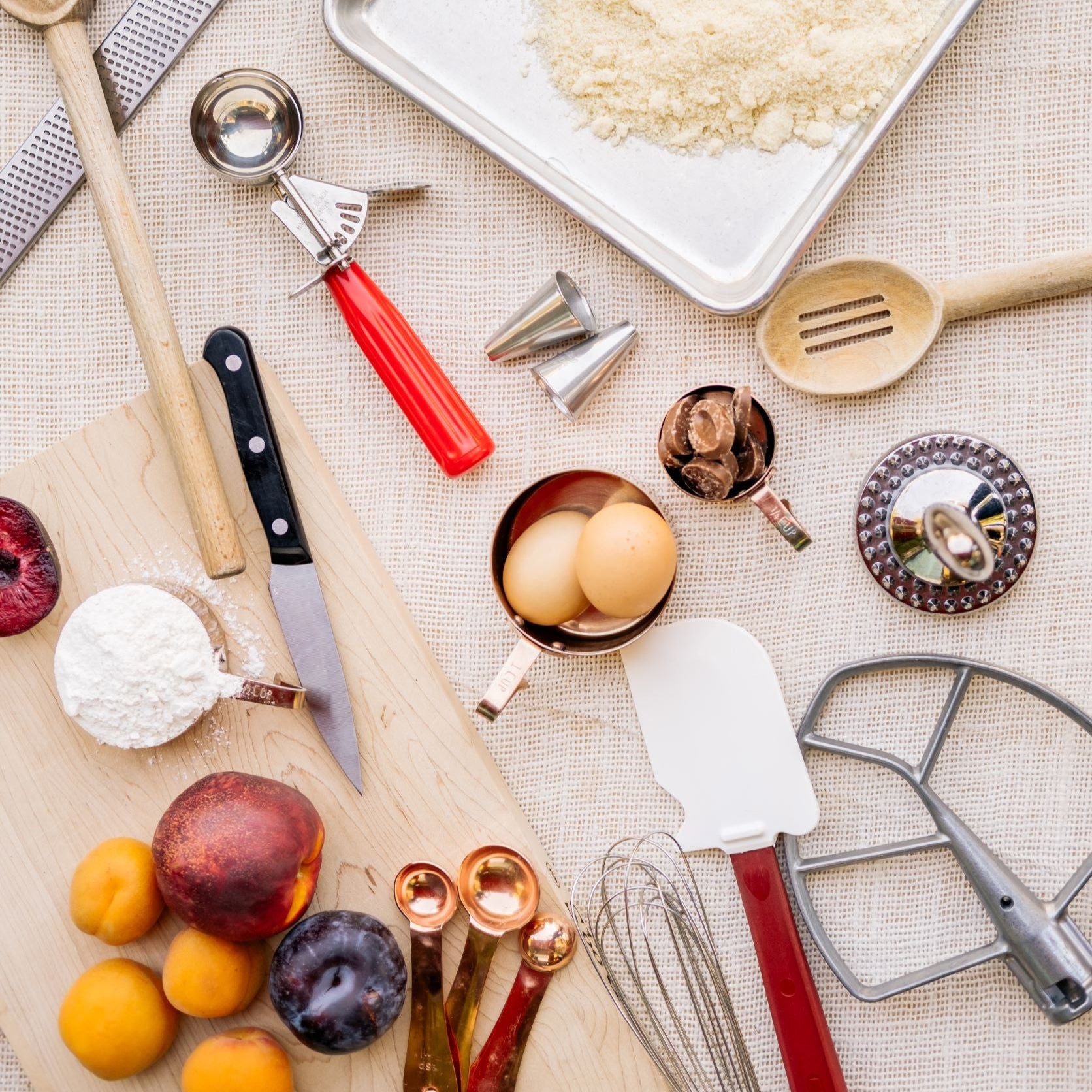 Assorted Baking utensils such as cutting boards, wooden spoons, measuringspoons, and scale on light burlap background