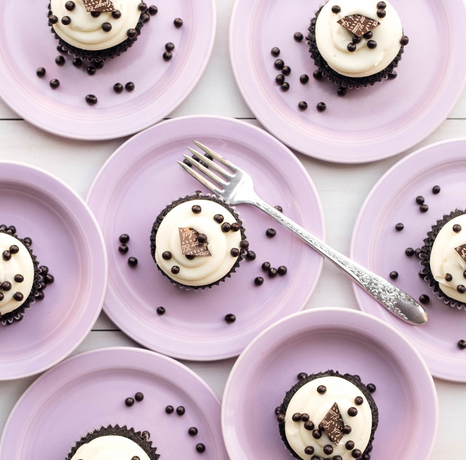 Red Velvet Cupcakes with cream cheese frosting, chocolate pears on pink plates with silver fork on center plate over white background